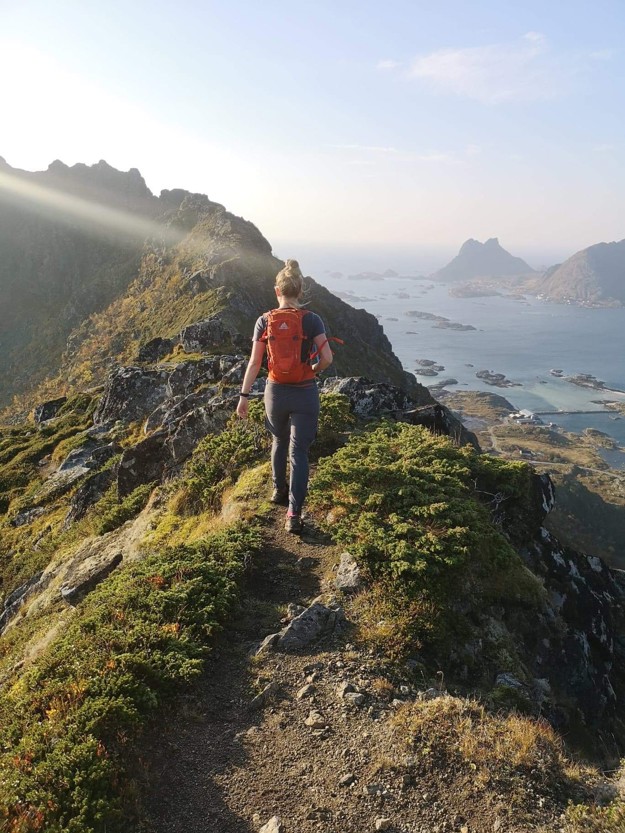 Astrid vendt med ryggen til kameraet på en bratt fjelltopp. 