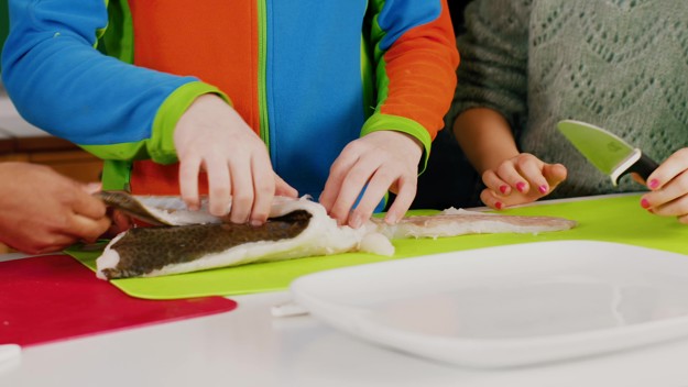 Children is filleting fish at the kitchen 