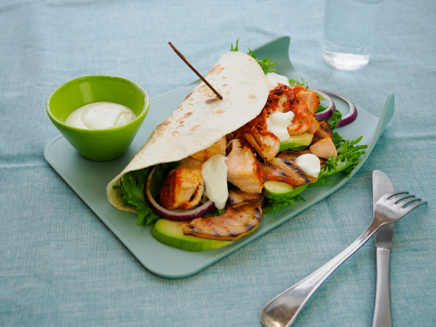 Wrap på lyseblå bakgrunn. Inni er det stekte laksebiter, paprika, papaya og rømmedressing