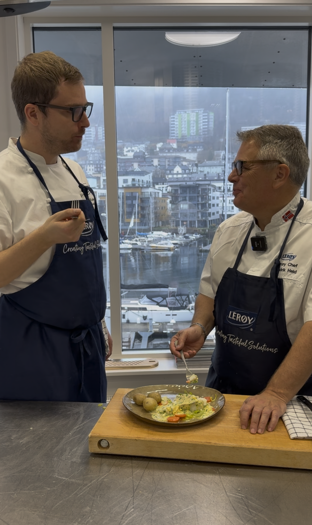 To menn ser på hverandre, begge med Lerøy-forklær, foran dem står et fat mer persetorsk